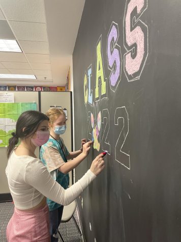 CLASSY ART--Seniors Hannah Seratte and Gracen Russell, both AP Art students, decorate the Class of 22 Signing Wall in the library. It will be enough of the college experience away from home for me, said Seratte, who plans to attend university in-state, but I can still travel easily to see family. Last year, 93 percent of the DM graduating Class of 2021 attended post-secondary education (73 percent attended university and 20 percent a two-year institution), according to Ms. Dorsch, DMs college and career counselor. 