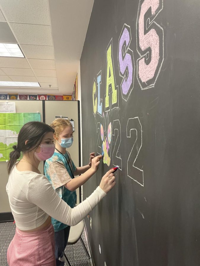 CLASSY+ART--Seniors+Hannah+Seratte+and+Gracen+Russell%2C+both+AP+Art+students%2C+decorate+the+Class+of+22+Signing+Wall+in+the+library.+It+will+be+enough+of+the+college+experience+away+from+home+for+me%2C+said+Seratte%2C+who+plans+to+attend+university+in-state%2C+but+I+can+still+travel+easily+to+see+family.+Last+year%2C+93+percent+of+the+DM+graduating+Class+of+2021+attended+post-secondary+education+%2873+percent+attended+university+and+20+percent+a+two-year+institution%29%2C+according+to+Ms.+Dorsch%2C+DMs+college+and+career+counselor.+