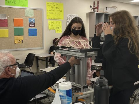 DOOMED TO FALL - Mr. Johnson assisting freshman Giana Despirito and Luca Collins with their bridge testing. My favorite part of this project was creating the design of the bridge, says Giana. They have been performing the bridge project for over 32 years. 