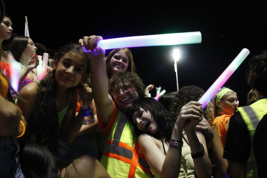 GLOWING WITH SPIRIT: The Wolfden student section shines bright with smiles and glowsticks for an exciting homecoming game with a huge turnout. Many wolves wear construction vests in honor of the neon theme. Inside the crowd, seniors Caden Gereb, Emma Modrich, Sofia Lauricella, and Jordan O’Leary show their spirit and what the student section culture is like for those who aren’t as encapsulated into the game of Football. “To be honest, I never really heard of the other school. It’s kinda cool we won though. Good for us,” says Student Council President Caden Gereb. Even those students who dont football games to watch the sport are nonetheless able to enjoy spending time with their friends and supporting school spirit. 
